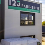 Panneau imprimé 123 Pare-Brise posé au-dessus d'une fenêtre, illustrant notre expertise en déploiement multi-sites sur le site de Décines.