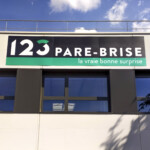 Panneau avec logo 123 Pare-Brise installé au-dessus d'une fenêtre, dans le cadre du déploiement multi-sites à Décines.