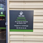 Zoom sur le panneau d'horaires situé à côté de l'entrée et de l'enseigne LightBox du magasin DO&KA de Chatte.