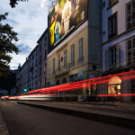 Plan de côté nocturne valorisant le trompe-l'œil et l'intégration respectueuse de la campagne grand format sur la façade de la place Bellecour à Lyon.