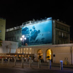 Publicité sur échafaudage à Nice de nuit – Toile microperforée Samsonite illuminée sur le Palais Hongran, face à la mer Méditerranée