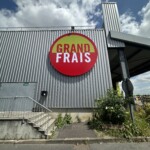 Enseigne lumineuse ronde Grand Frais rénovée sur la façade métallique d'un magasin.