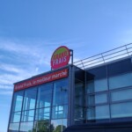 Enseigne ronde Grand Frais posée sur le toit de la structure vitrée du magasin.