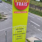Totem d'entrée de parking Grand Frais rénové au bord d'une route.