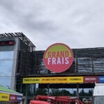 Enseigne circulaire Grand Frais fixée sur le bardage bois d'un supermarché.