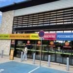 Enseigne circulaire Grand Frais fixée sur le bardage bois d'un supermarché.